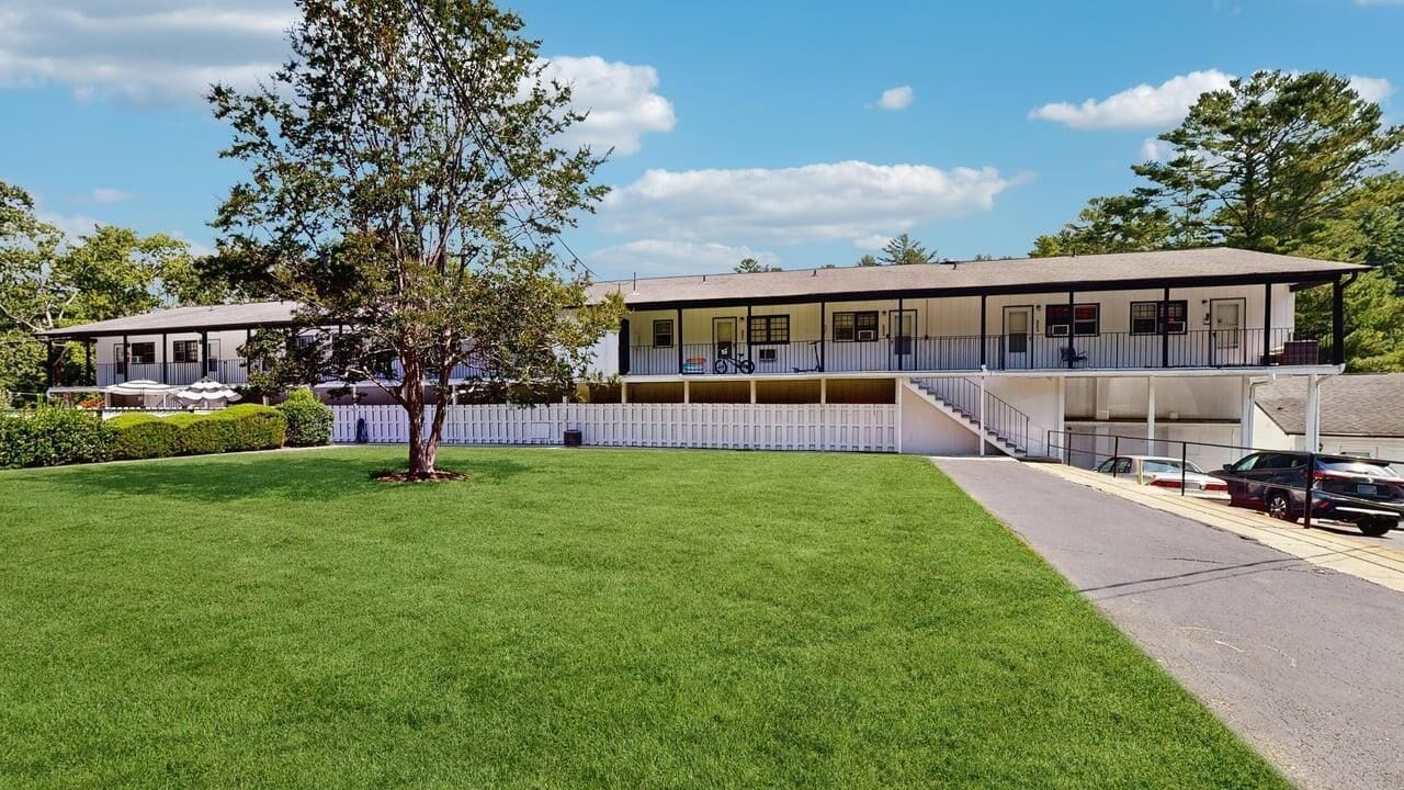A two-story building with a flat roof, a balcony on the upper floor, and a covered outdoor area.