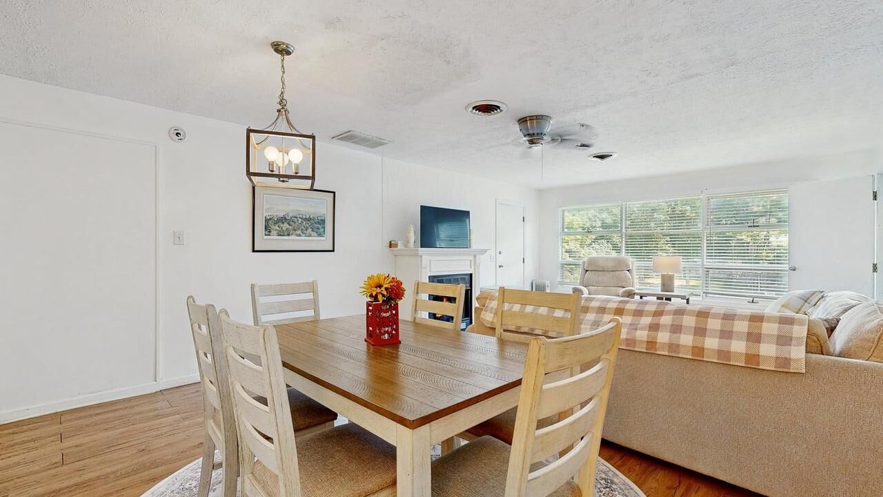 A dining area with a wooden table and chairs, a chandelier, and a sofa with a checkered throw.