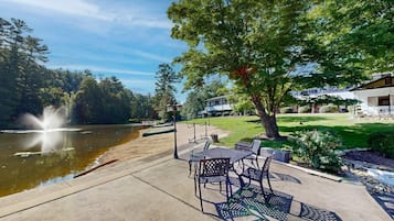 A lakeside patio with outdoor seating, a fountain, and a building in the background.