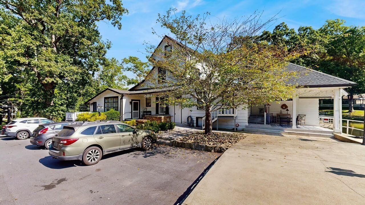 A two-story building with a covered porch and a parking area with cars.