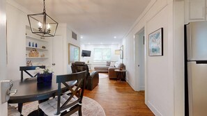 A modern living room with a sofa, a dining table with chairs, a television, and a refrigerator.