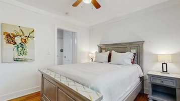 A bedroom with a bed, bedside tables, a ceiling fan, and a painting on the wall.