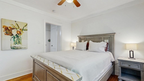 Une chambre à coucher avec un lit, des tables de chevet, un ventilateur de plafond et un tableau accroché au mur.
