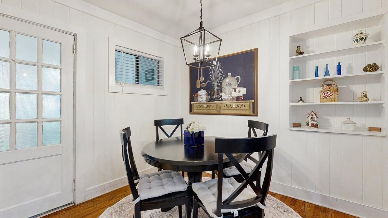 A dining room with a round table, black chairs, a chandelier, and white paneled walls.