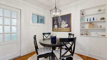 A dining room with a round table, black chairs, a chandelier, and white paneled walls.