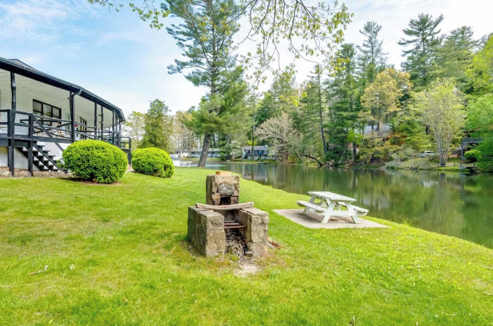 A lakeside property with a stone fire pit, picnic table, and a building with a staircase.