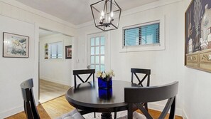 A dining area with a round table, black chairs, a blue vase with flowers, and a geometric chandelier.