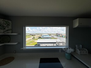 A room with a large window overlooking a water body and buildings, a kitchen counter, and a small rug. - Tranquil 1-bedroom bungalow with AC in Bolivar Peninsula (Bolivar Peninsula)