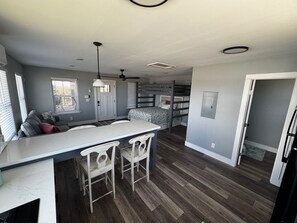 A modern kitchen with a central island, bar stools, a ceiling fan, and a built-in bench with storage. - Tranquil 1-bedroom bungalow with AC in Bolivar Peninsula (Bolivar Peninsula)