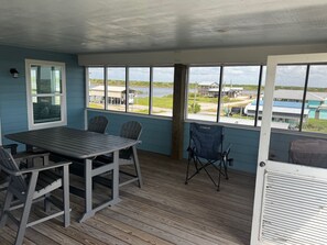 A covered patio with a table and chairs, large windows offering a view of the landscape, and a door with a window. - Tranquil 1-bedroom bungalow with AC in Bolivar Peninsula (Bolivar Peninsula)