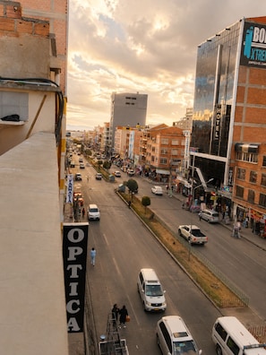 Vista de la calle con varios edificios, incluyendo un hotel con un letrero que dice 'HOTEL' y una farmacia con un letrero que dice 'OPTICA'.