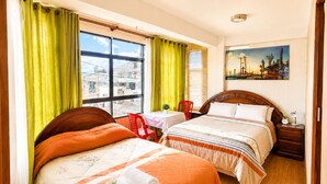 Habitación de hotel con dos camas, una ventana con cortinas, un cuadro en la pared y una pequeña mesa con una silla.