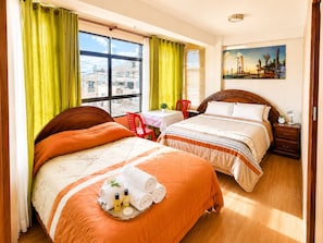 Habitación de hotel con dos camas, una ventana con cortinas, un cuadro en la pared y una pequeña mesa con una silla.