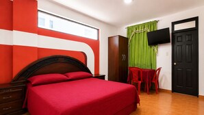 Una habitación de hotel con cama, escritorio, silla, televisor y armario.