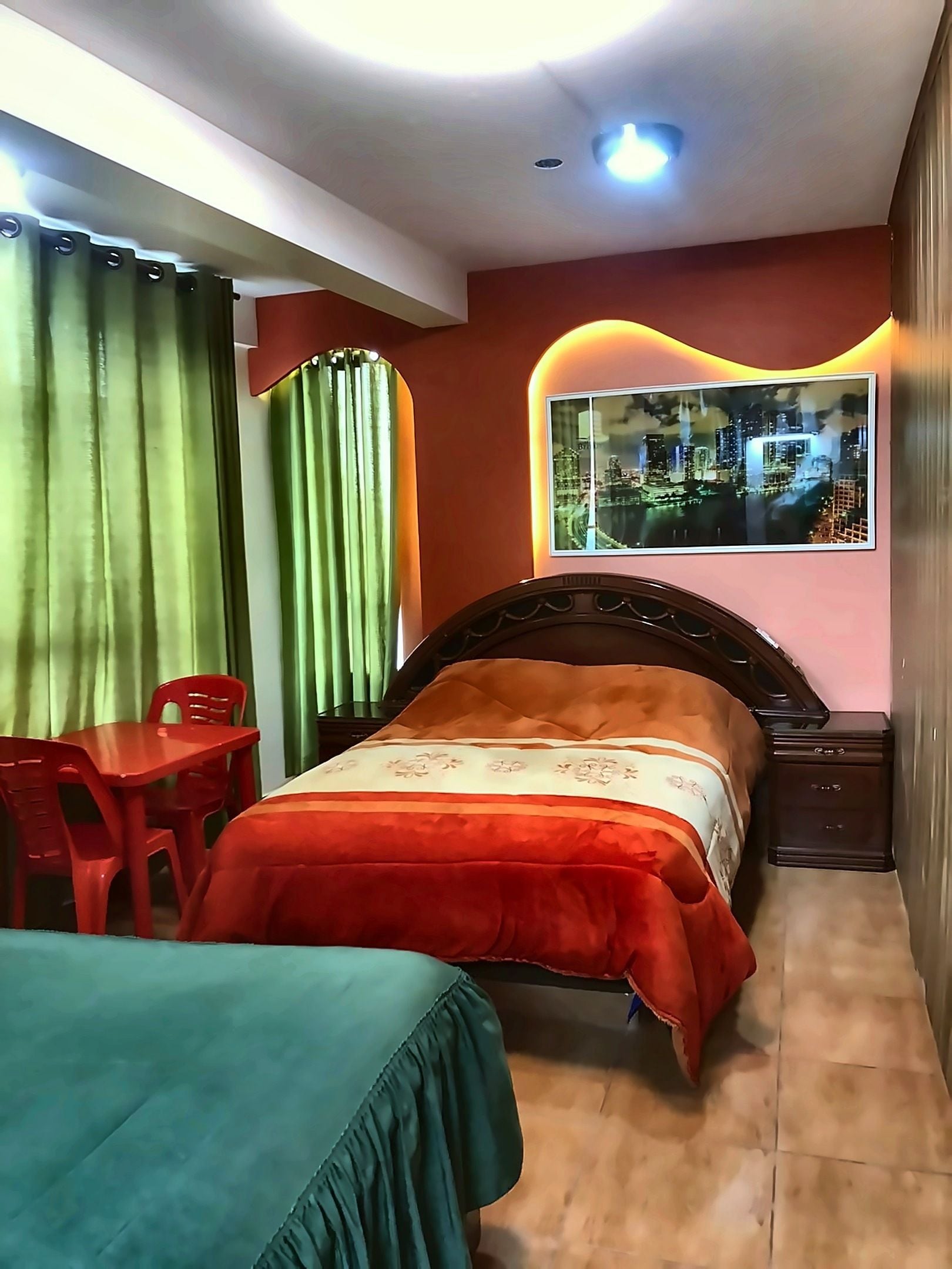 A bedroom with a bed, a desk, and a chair. There is a window with a view of buildings.