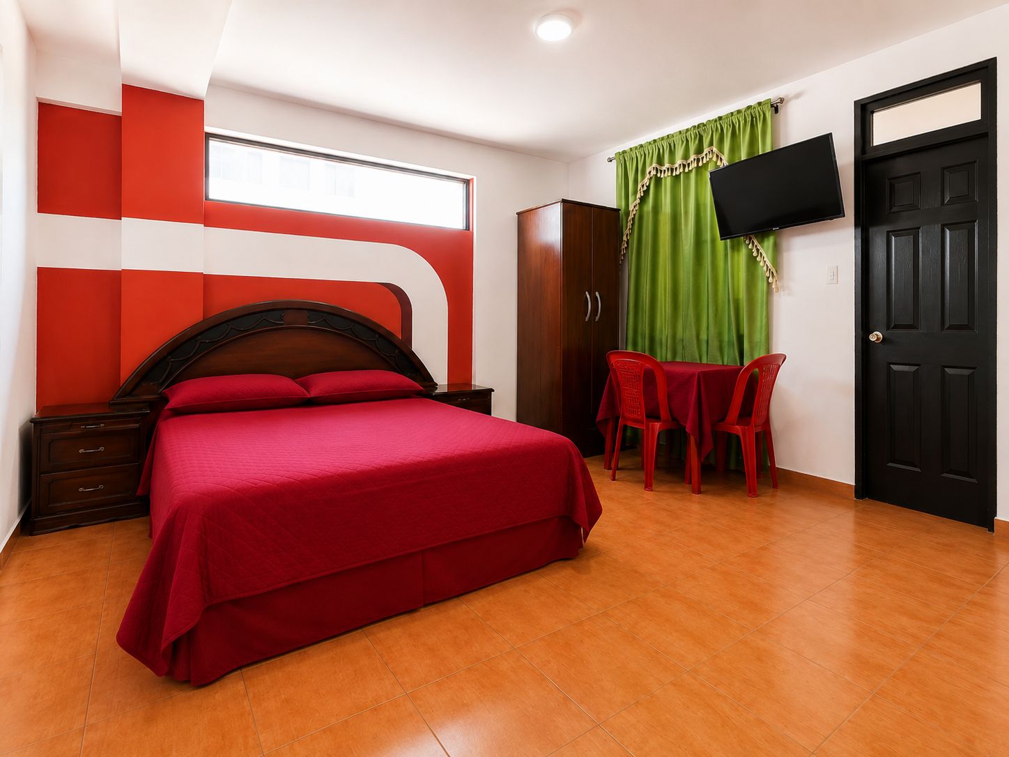A hotel room with a bed, a desk, a chair, a wardrobe, and a TV mounted on the wall.