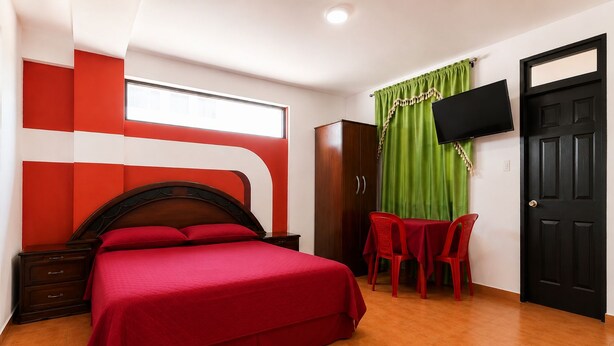 Habitación de hotel con una cama, un escritorio, una silla, un armario y un televisor montado en la pared.