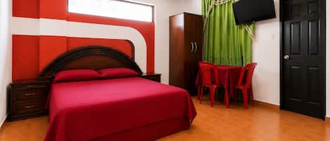 Habitación de hotel con una cama, un escritorio, una silla, un armario y un televisor montado en la pared.