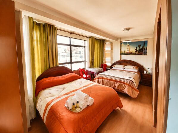 A hotel room with two beds, a window with curtains, a painting on the wall, and a bedside table with a lamp.
