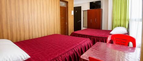 Una habitación de hotel con dos camas, una mesa, sillas, un armario y un televisor.