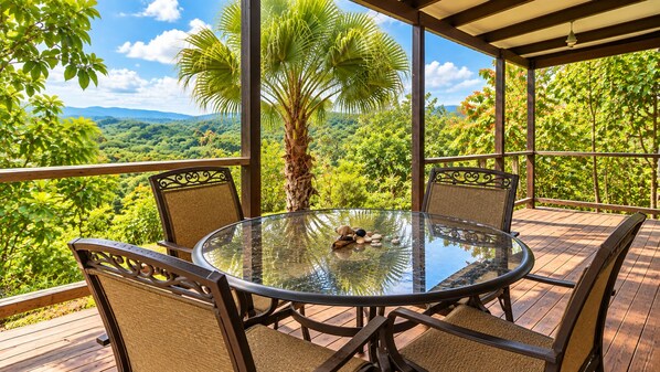 Una mesa redonda de vidrio con sillas, rodeada por una terraza de madera con vista a un paisaje boscoso.