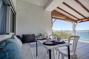 A balcony with a table set for two, a sofa, and a view of the sea. - Vrbo Property (Le Diamant)
