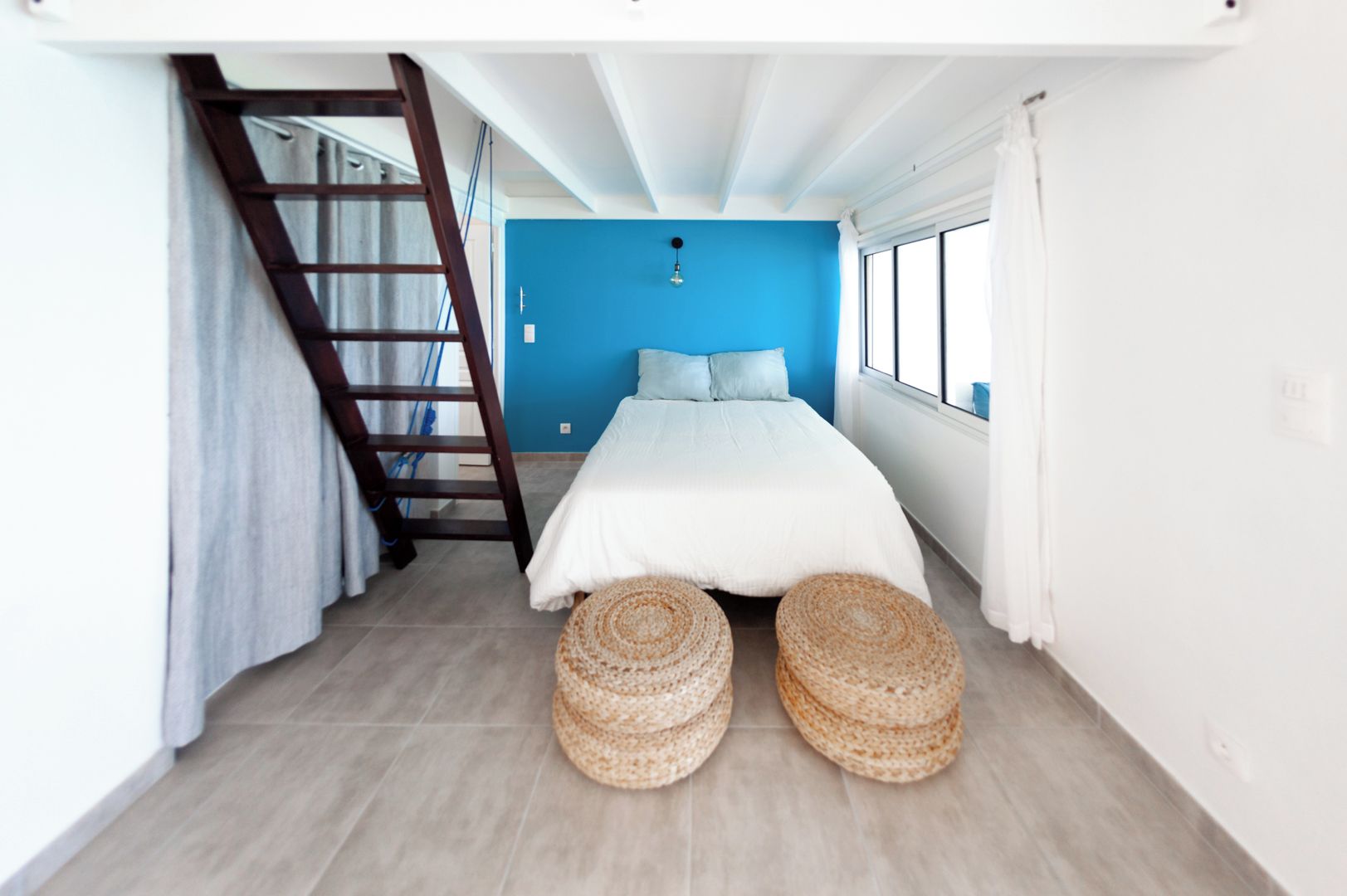 Een slaapkamer met een bed, een ladder en een raam.