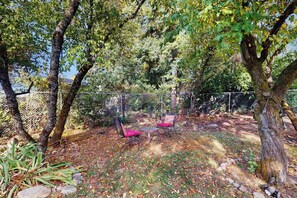 A fenced outdoor area with a table and two chairs, surrounded by trees and a rocky ground. - 3 BR peaceful sanctuary with piano and yard (Seattle)