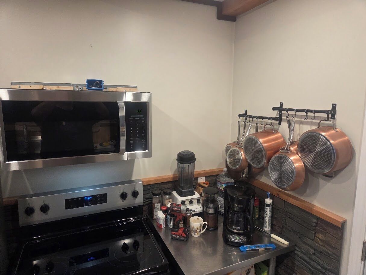 A kitchen with a microwave, stove, blender, and hanging copper pots.