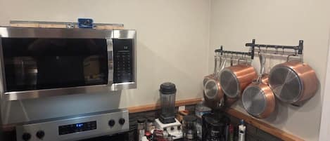 Una cocina con microondas, estufa, licuadora y ollas de cobre colgadas.