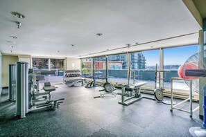 Ein Fitnessstudio mit Trainingsgeräten, großen Fenstern und Blick auf Gebäude.