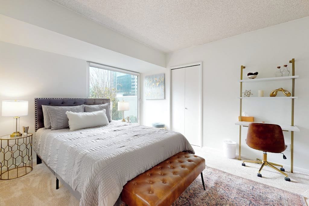 A bedroom with a large bed, a bench, a desk with a chair, and a shelving unit.