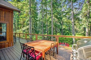 A wooden deck with a table and chairs, overlooking a forested area. - Welcoming 2BR Lakeview - Deck - Firepit - Washer Dryer (Anderson Island)