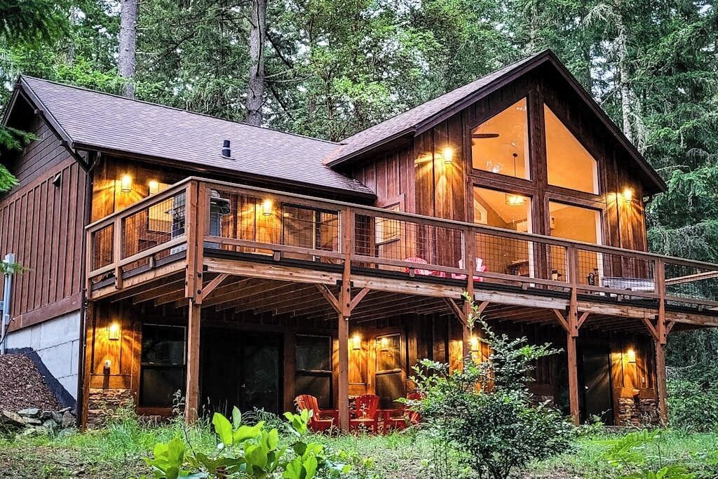 A two-story wooden cabin with a balcony, surrounded by forest.