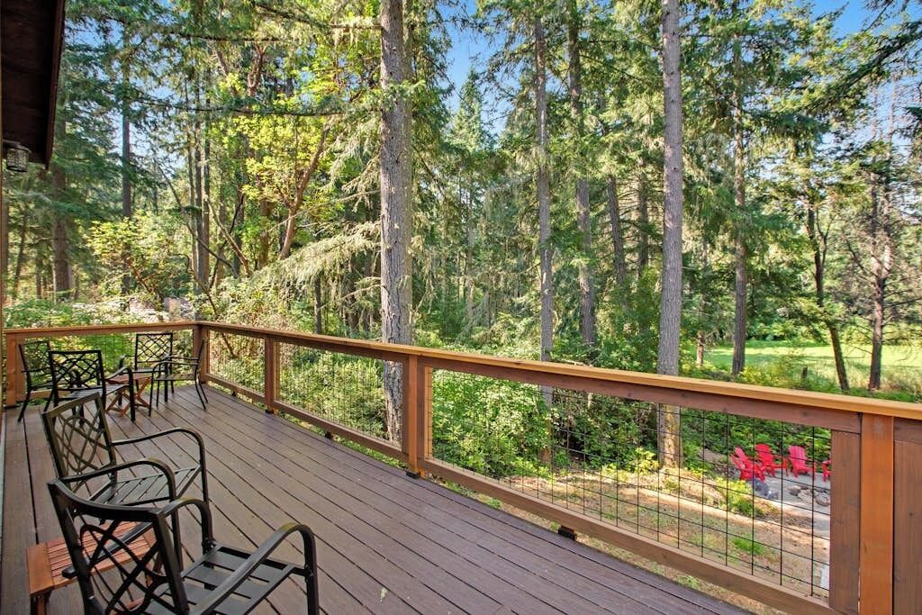 Une terrasse en bois, dotée de chaises en métal et d’une rambarde, qui offre une vue sur une zone boisée.