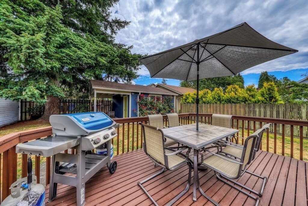 A deck with a grill, table, chairs, and an umbrella.