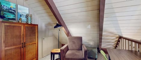 Une pièce avec un plafond en pente, une armoire en bois, une chaise, une petite table et une lampe.