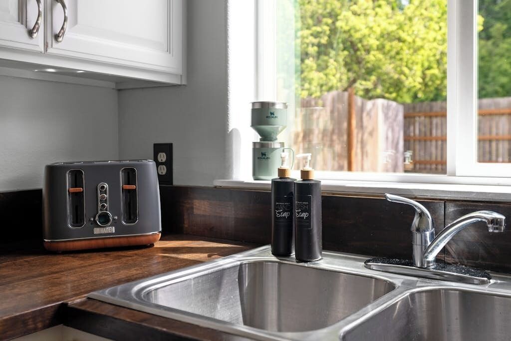 A kitchen with a toaster, two soap bottles, and a stainless steel sink.