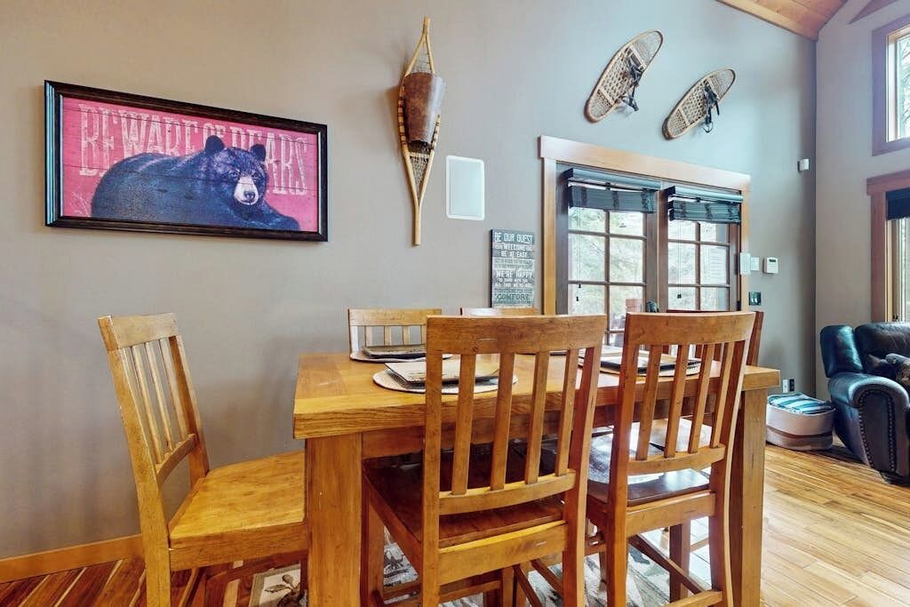 A dining area with a wooden table and chairs, a framed bear picture, and a wall-mounted decorative item.