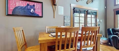 A dining area with a wooden table and chairs, a framed bear picture, and a wall-mounted decorative item.