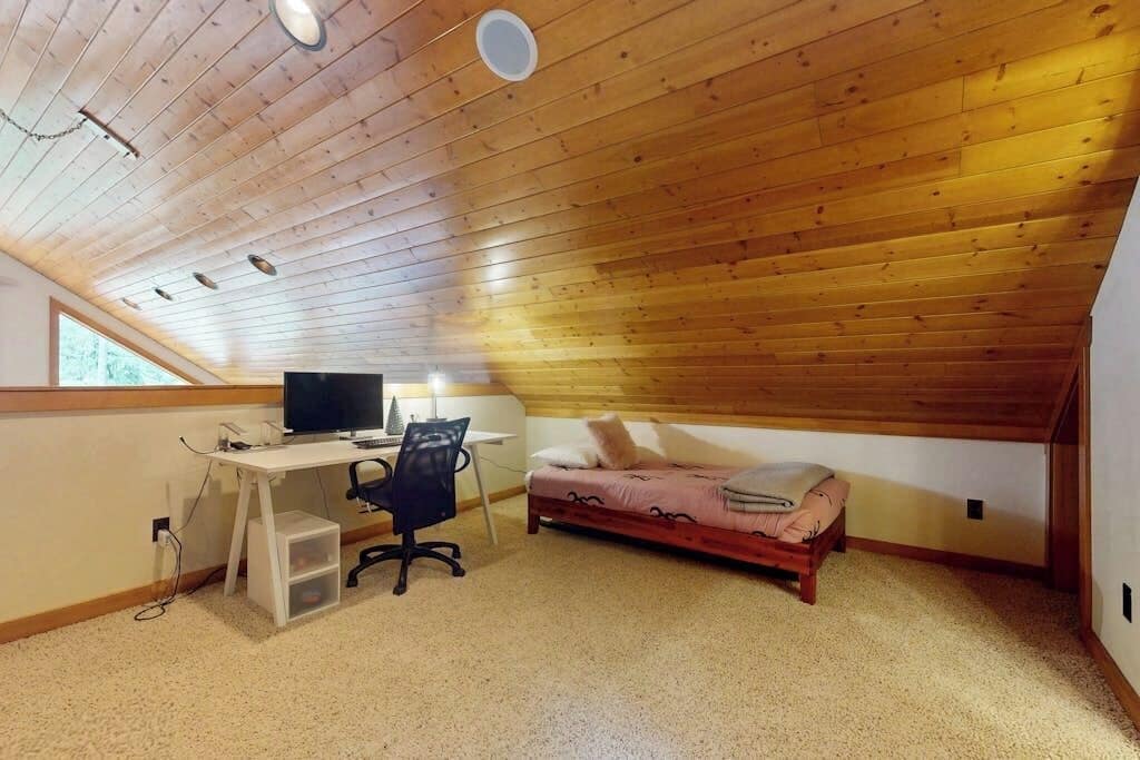 Ett rum med ett sluttande tak, en säng, ett skrivbord med en dator och en stol.