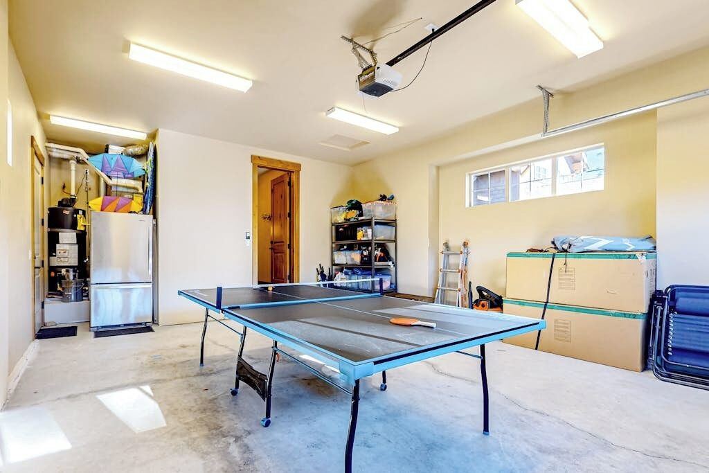 Una habitación con mesa de ping-pong, proyector y ventana con persianas.