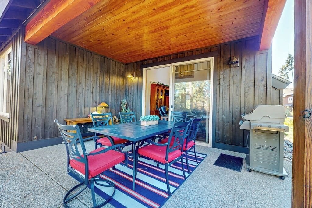 Une terrasse extérieure dotée d’un plafond en bois, d’une table à manger avec des chaises et d’un barbecue.