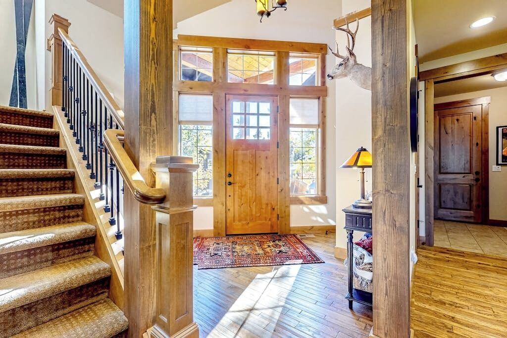 Un hall d’entrée spacieux avec un escalier en bois, une grande porte en bois et un tapis au sol.