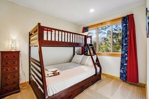 Ein Etagenbett mit Holzrahmen und weißer Bettwäsche, eine Kommode mit mehreren Schubladen und ein Fenster mit roten Vorhängen.