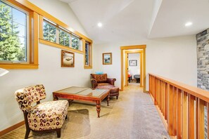 A spacious hallway with a wooden railing, a patterned armchair, a leather sofa, and a glass-top coffee table. - Dog-friendly 4BR with hot tub, game room & patio (Cle Elum)