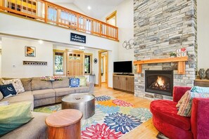 A spacious living area with a fireplace, a sofa set, a coffee table, and a red armchair. - Dog-friendly 4BR with hot tub, game room & patio (Cle Elum)