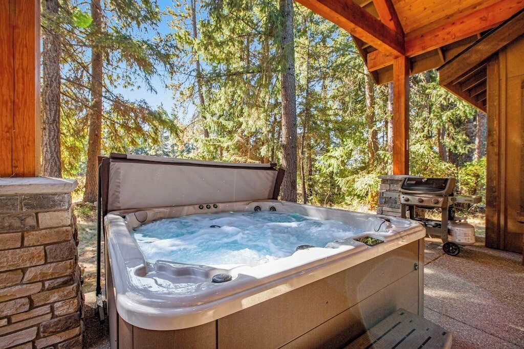 A hot tub in a wooded area with a stone wall and a grill.