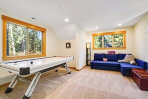 Ein Zimmer mit Pooltisch, blauem Sofa und großen Fenstern mit Blick auf Bäume.