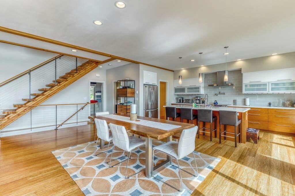 Une cuisine moderne dotée d’un îlot central, d  ’un escalier en bois et d’un coin repas agrémenté d’un tapis à motifs.